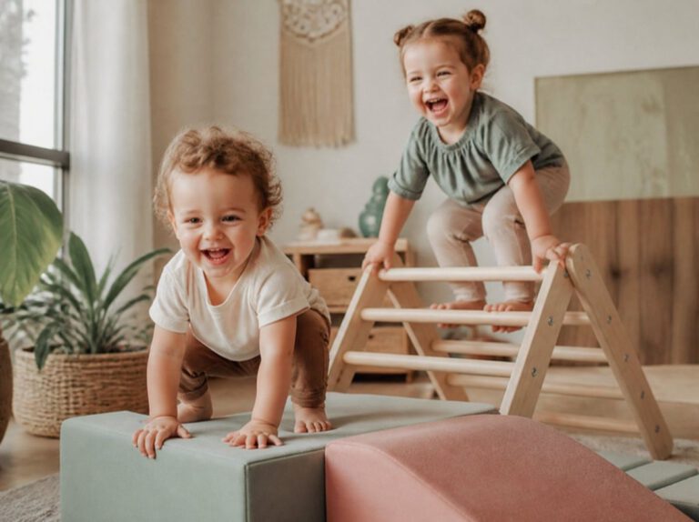 Zwei Kleinkinder klettern lachend auf Schaumstoffelementen und Pikler-Dreieck